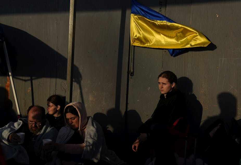 Men and women huddled together near the U.S. border near a yellow and blue Ukrainian flag.
