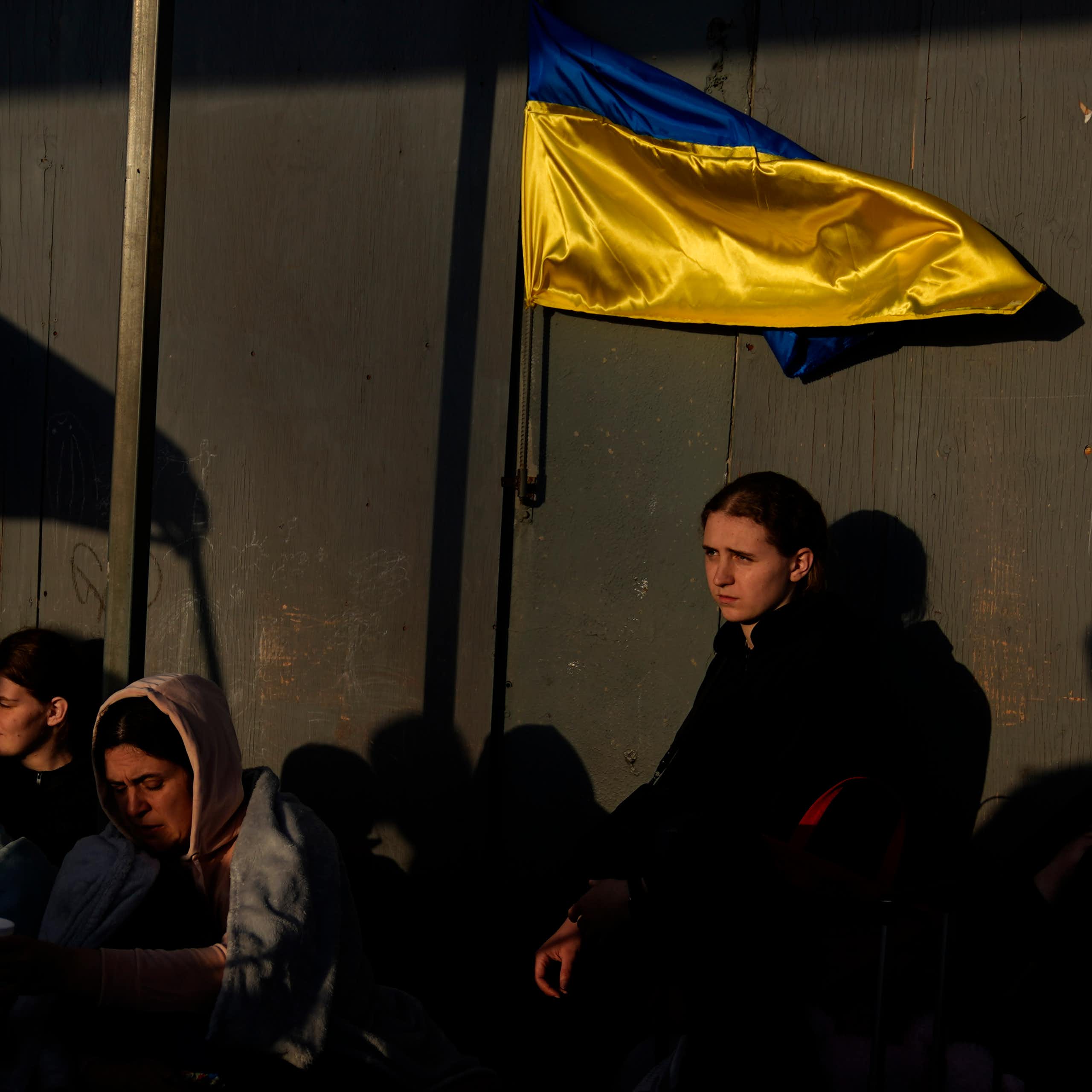 Men and women huddled together near the U.S. border near a yellow and blue Ukrainian flag.