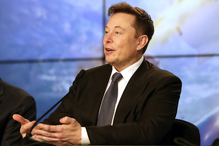 a man in a dark business suit gestures with both hands together in front of him as he speaks into a microphone
