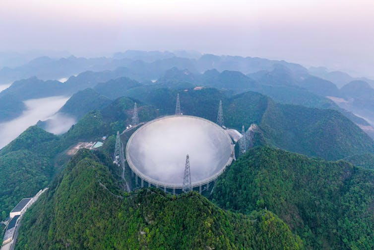 A giant spherical dish-shaped telescope on the top of a mountain.