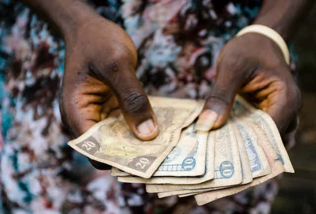An African woman holds several bills in her hands.