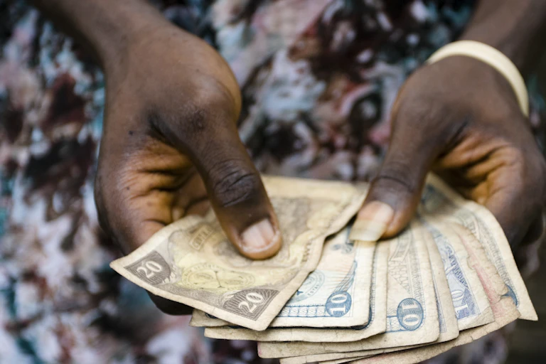 An African woman holds several bills in her hands.