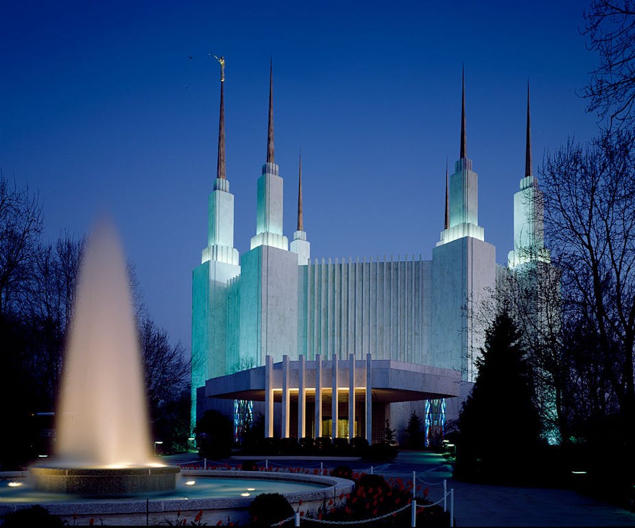 A white building with six tall spires behind a fountain.