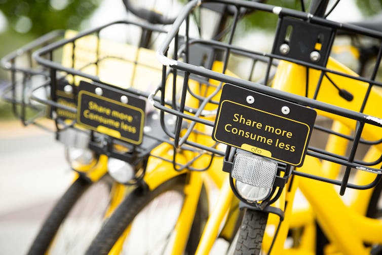 Close-up photo of two yellow bikes with front baskets, each with a sign reading, Share more Consume less.