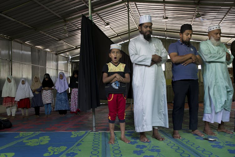 Muslims stand while praying inside a structure with metal walls.