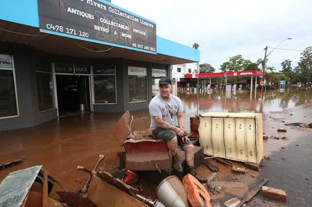 man sits on ruined furniture on flooded street
