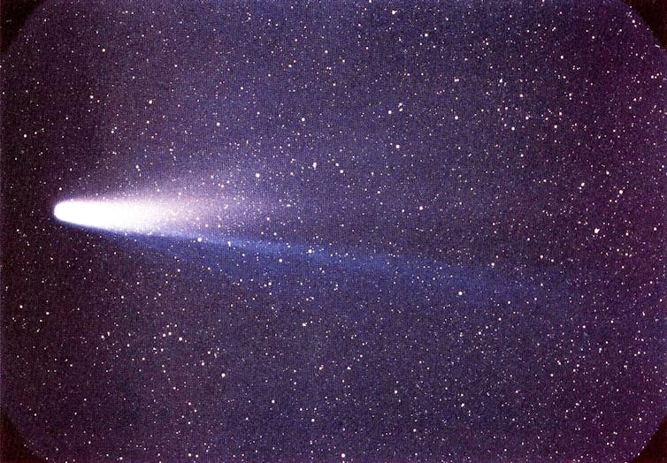 Comet Halley, as seen in 1986. The head of the comet is to the left, with the blue gas tail pointing to the lower right, and the dust tail curving slightly towards the upper right.