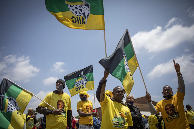 People wearing yellow shirts and carrying flags in black, green and yellow colours with letters ANC