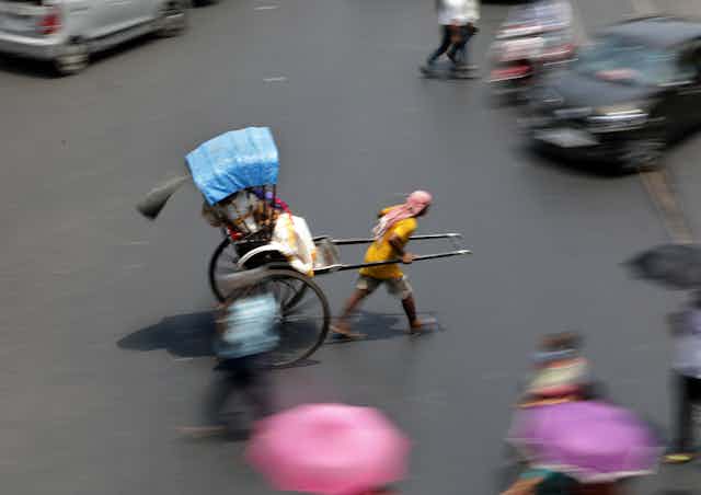 A man pulls a rickshaw across a busy intersection.