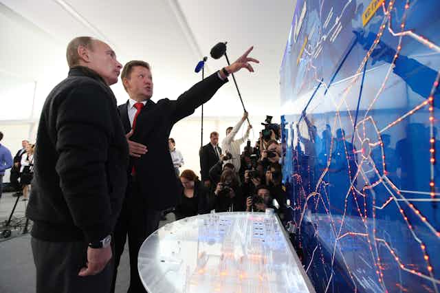 Putin looks at a video display while another man gestures to it