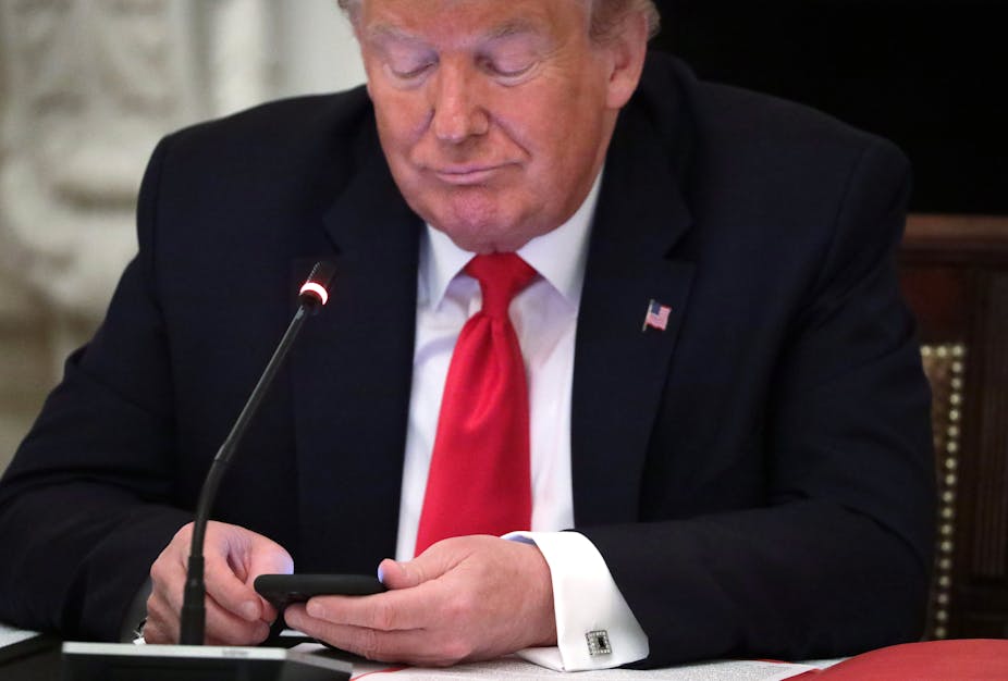 Donald Trump wearing a dark suit and red tie looks at his phone.