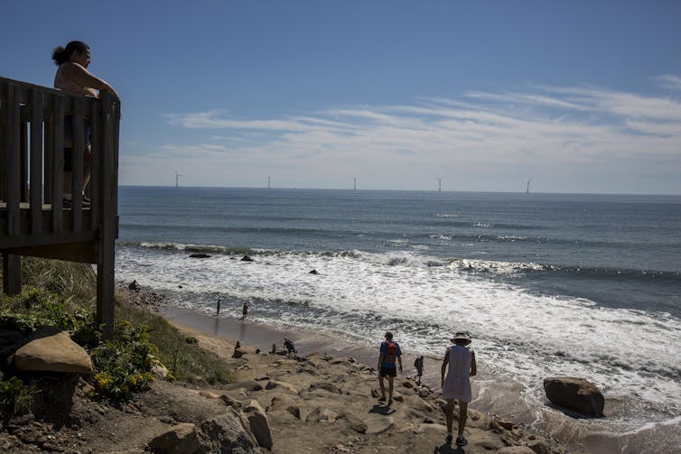 Tourists play on a beach with the Block Island Wind Farm in the distance.