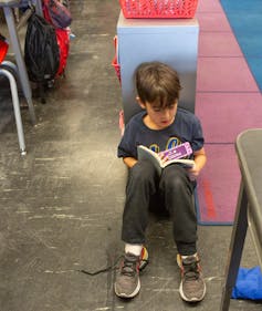 A boy sits on the floor in a classroom reading.