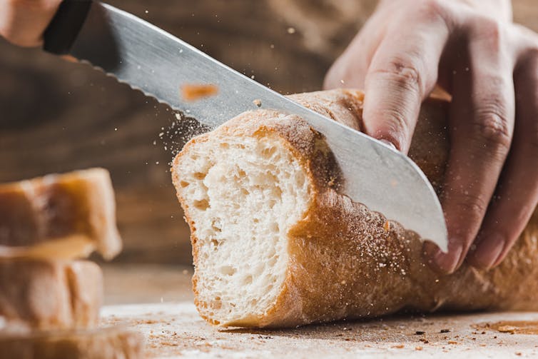 Cutting a baguette with a bread knife on chopping board