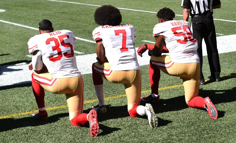 Three American football players kneel in protest.