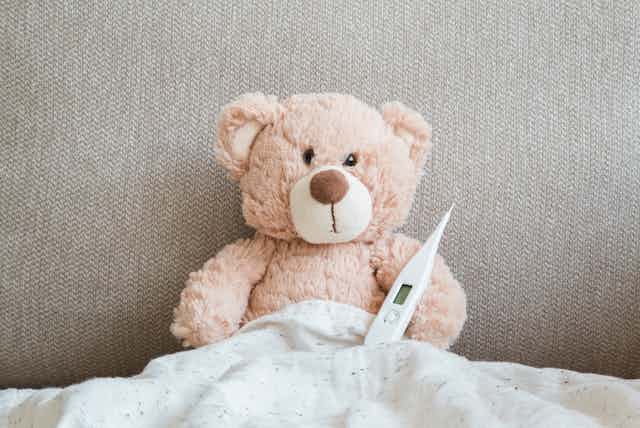 Sick teddy in bed with thermometer