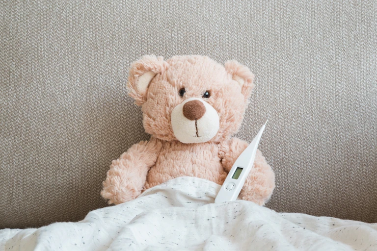 Sick teddy in bed with thermometer