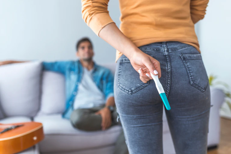 Woman about to tell male partner she's pregnant, holding test behind back