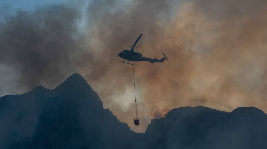 A helicopter carrying water in the middle of fire and smoke.