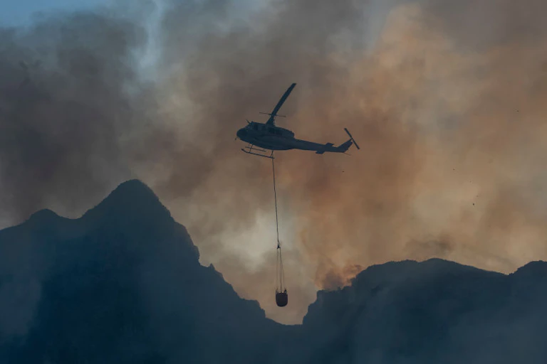 A helicopter carrying water in the middle of fire and smoke.
