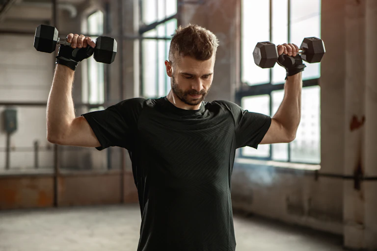 Young man performs an overhead press using two dumbbells.