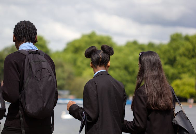 Three teenagers in school uniform walk away from the camera, outside.