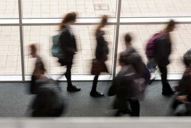 Secondary school pupils moving by a window in a school UK, blurred movement.