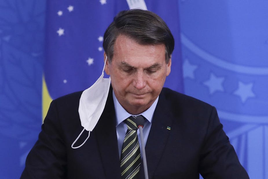 Le président brésilien est à une tribune, le masque pendant à une oreille.