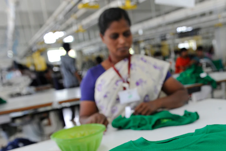 Woman sitting at factory table with piles of T-shirts