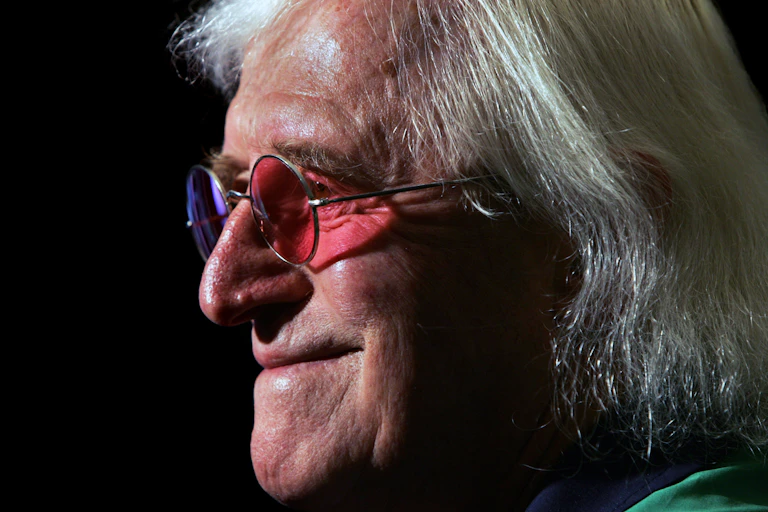 Close-up profile photo of Jimmy Savile in old age wearing round sunglasses with different coloured lenses