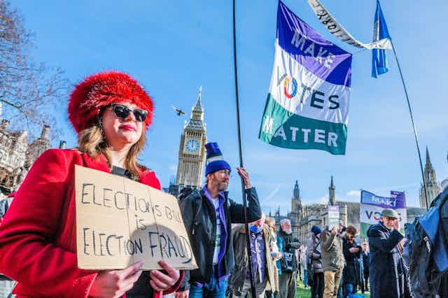 Woman in red holding placard against election bill with protesters in front of UK parliament