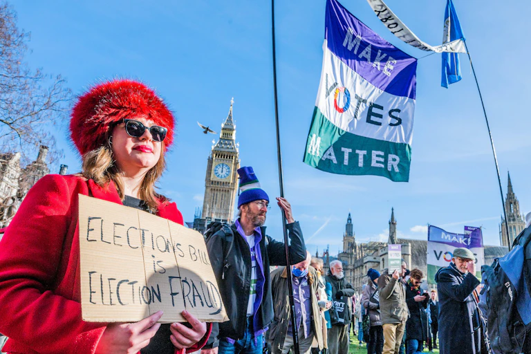 Woman in red holding placard against election bill with protesters in front of UK parliament