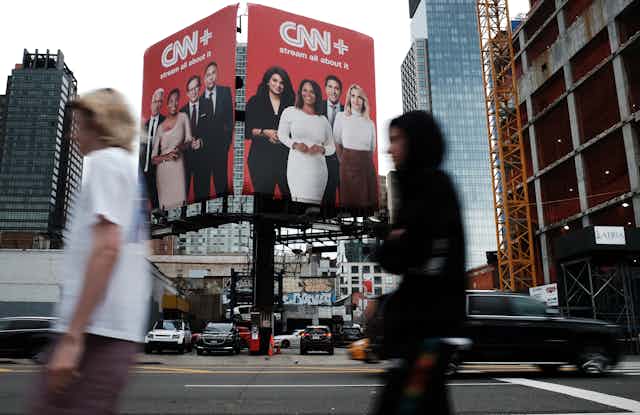 Pedestrians walk by a billboard advertising CNN+.