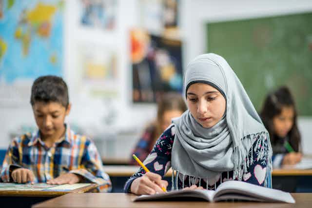 A Muslim student reads a book in class. 
