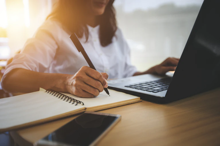 jeune femme prend des notes pendant qu'elle regarde un écran d'ordinateur