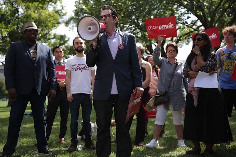 Man speaks into megaphone before crowd of protesters.