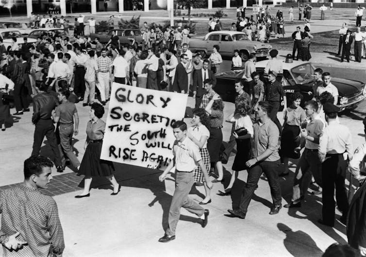 Hundreds of white people are protesting on a street against racial integration.