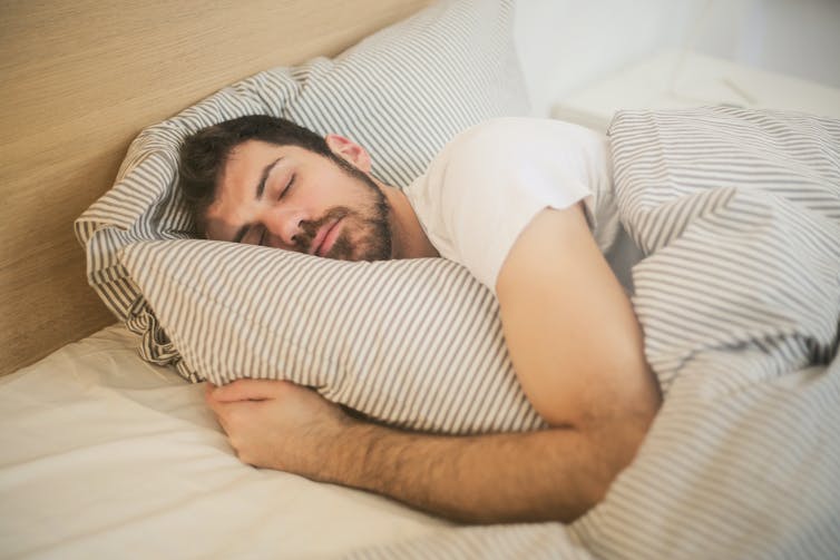 Un hombre durmiendo en la cama con un edredón de rayas azules y blancas.
