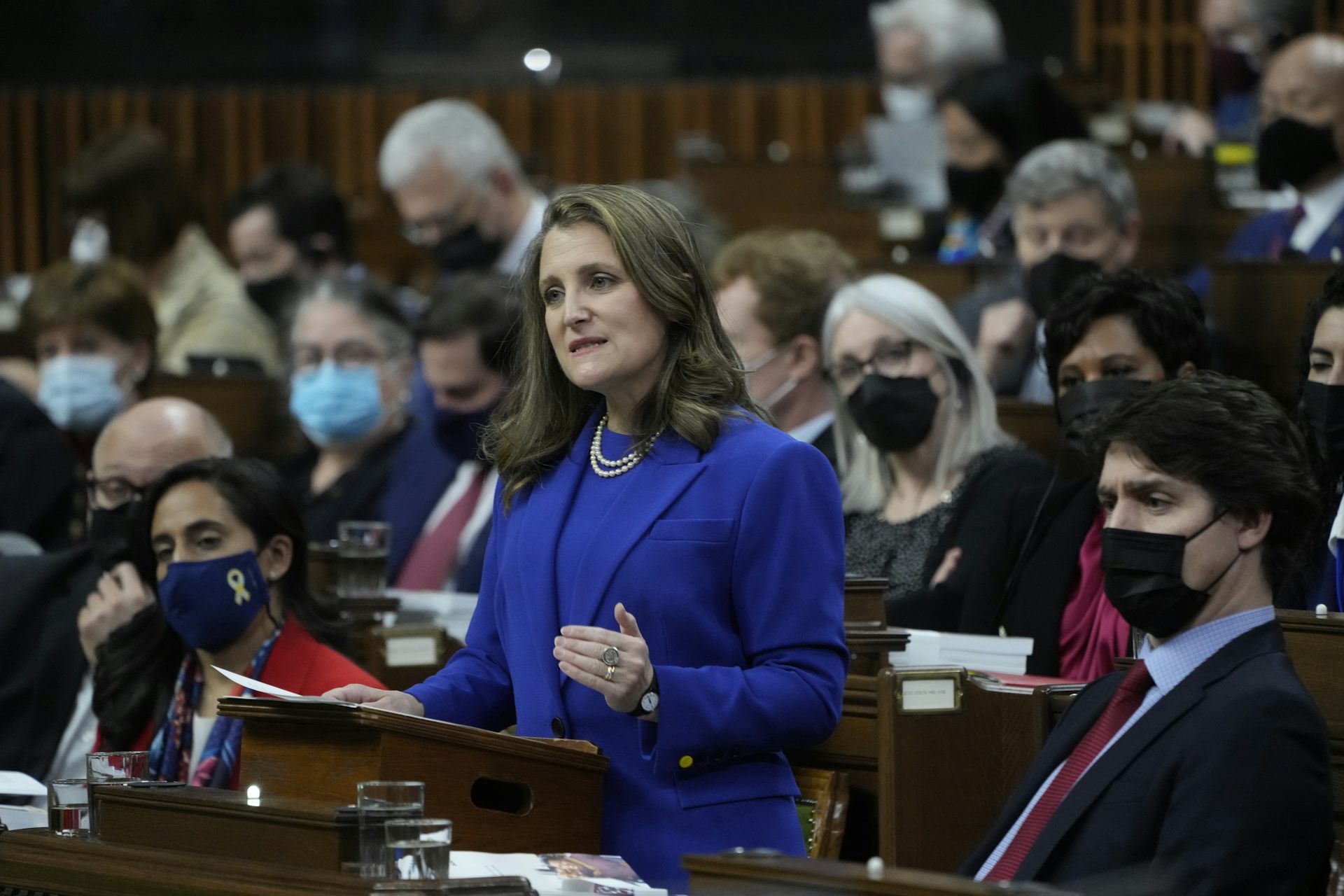 A woman in a blue suit stands at a lectern with people seated behind her
