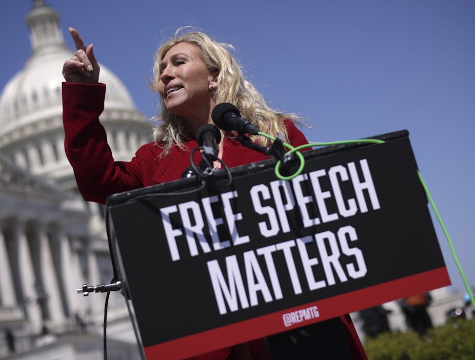 A white woman stand outside the U.S. Capital holding a sign that reads 'Free Speech Matters'