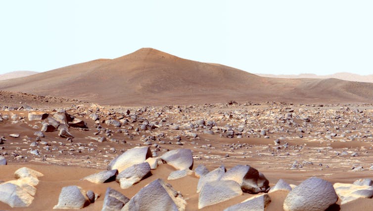 Empty landscape with rocks in the foreground and sandy hills in the background.