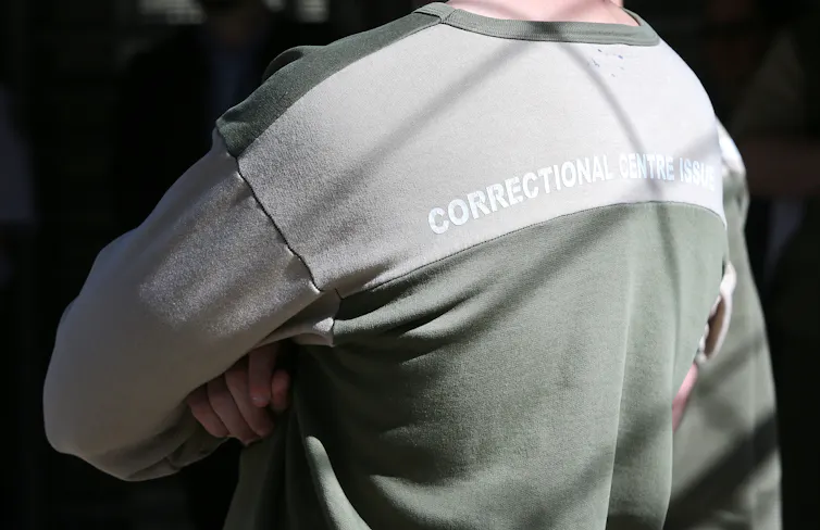 A man wearing a shirt saying 'correctional centre issue' faces away from the camera.