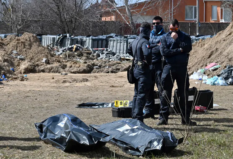 Des gendarmes se tiennent à côté de corps dans des sacs et du matériel d’annotation de la zone