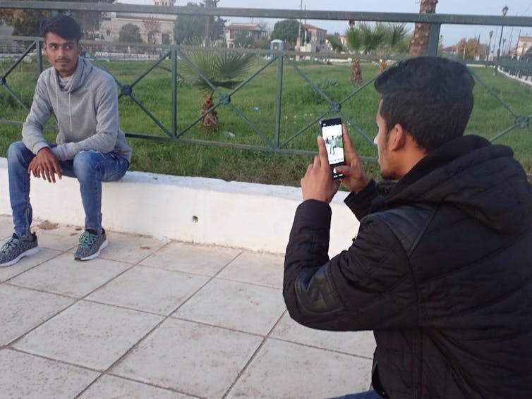 A man takes a photo of another man on his mobile phone