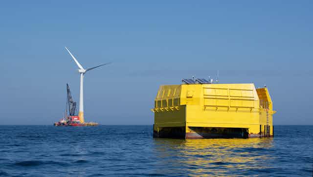 Deux infrastuctures prises en pleine mer : un gros cube jaune et une éolienne
