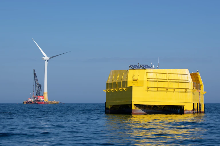Deux infrastuctures prises en pleine mer : un gros cube jaune et une éolienne