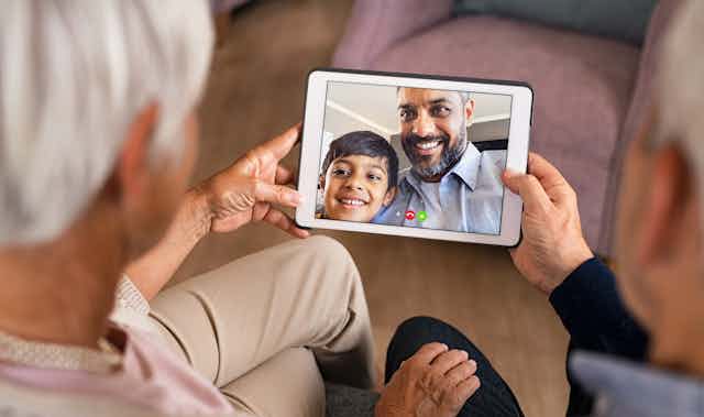 A tablet with a father and son is being held by two older adults.