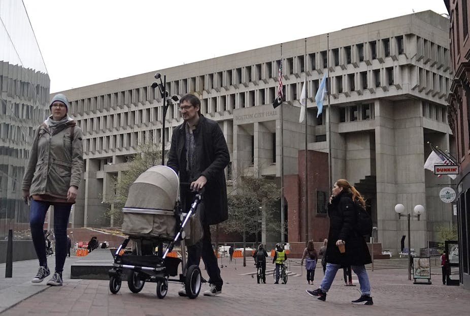 A man and woman walk a stroller in front of a large grey government building.