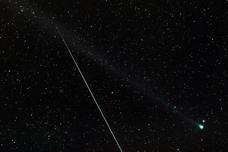 Comet C/2020 F8 (SWAN) stretching from bottom right (with a green head) to top left (with a long thing tail), joined by an Eta Aquariid meteor, stretching from the bottom of the image to the centre of the frame