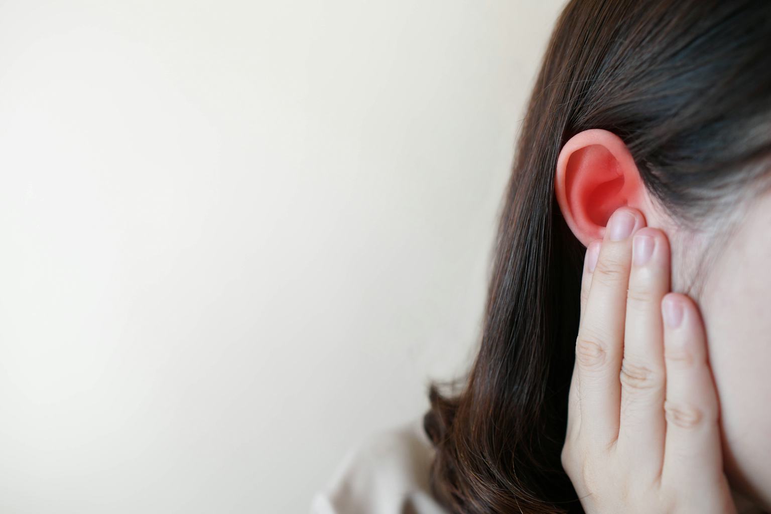 Close-up of a woman touching her reddened ear, indicating ear discomfort